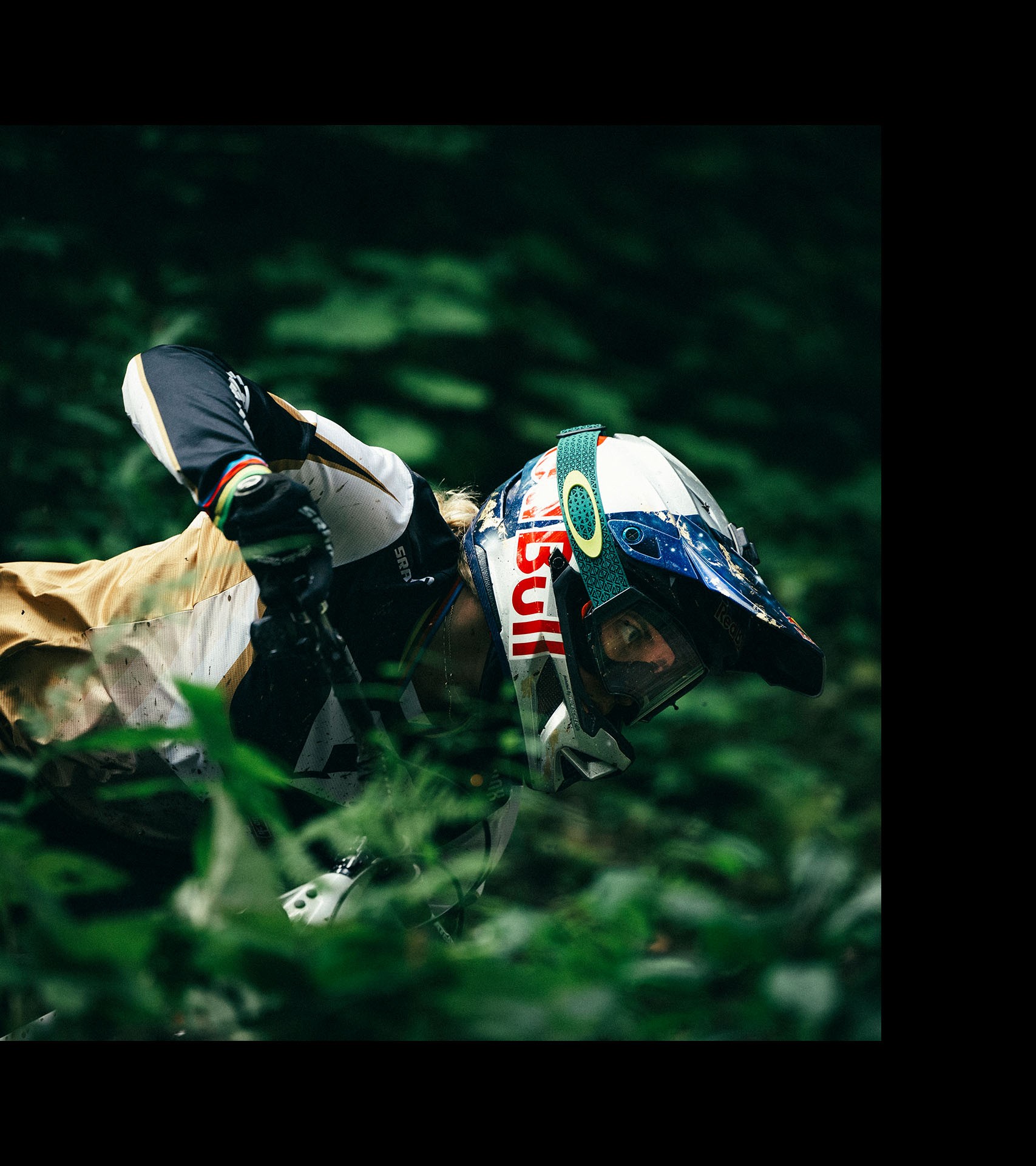Vali in full gear and protective helmet looks focused as she manoeuvres her bike, framed by lush green foliage.